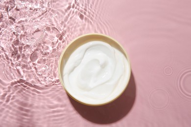 Cosmetic product. Jar with cream in water on pink background, top view