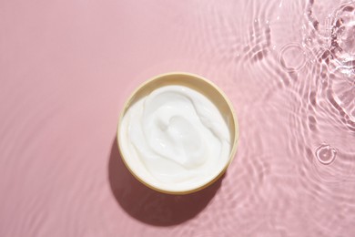 Photo of Cosmetic product. Jar with cream in water on pink background, top view