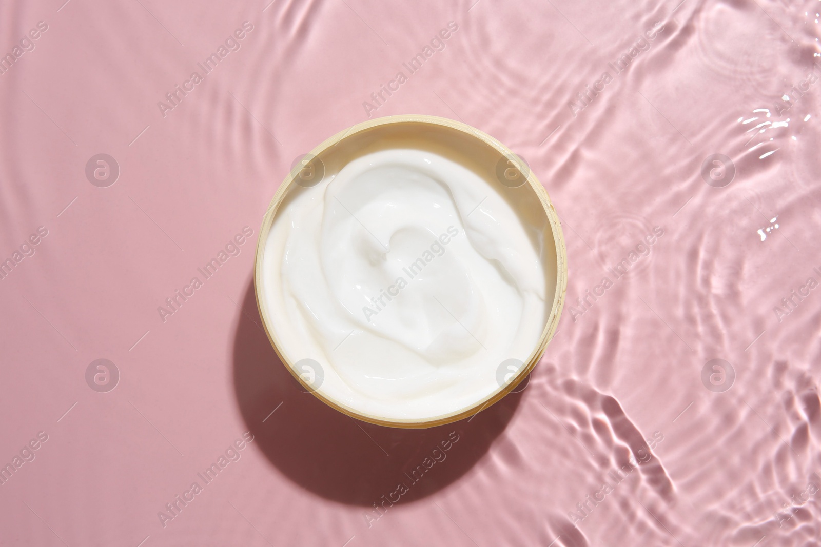 Photo of Cosmetic product. Jar with cream in water on pink background, top view