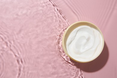 Cosmetic product. Jar with cream in water on pink background, top view. Space for text