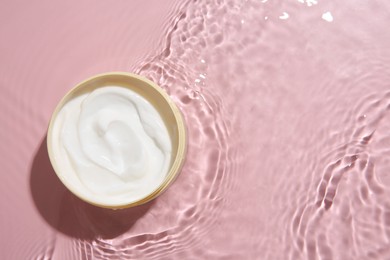 Cosmetic product. Jar with cream in water on pink background, top view. Space for text