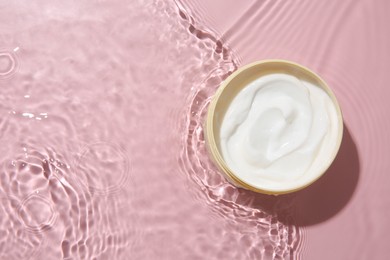 Photo of Cosmetic product. Jar with cream in water on pink background, top view. Space for text