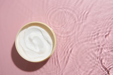 Photo of Cosmetic product. Jar with cream in water on pink background, top view. Space for text