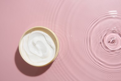 Photo of Cosmetic product. Jar with cream in water on pink background, top view. Space for text