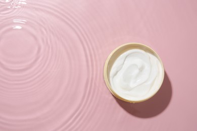 Photo of Cosmetic product. Jar with cream in water on pink background, top view. Space for text