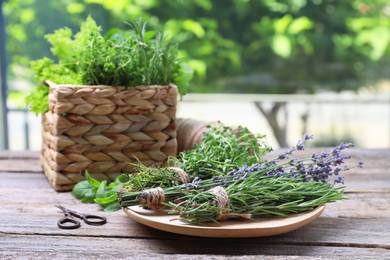 Photo of Different aromatic herbs and scissors on wooden table against blurred background