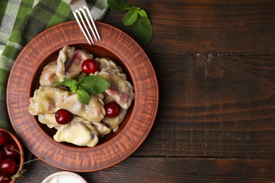 Photo of Traditional Ukrainian dumplings (varenyky) with cherries served on wooden table, flat lay. Space for text