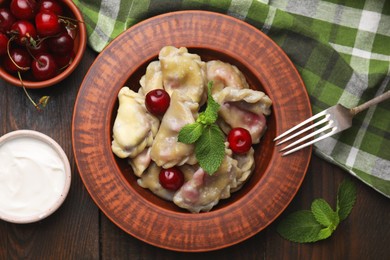 Photo of Traditional Ukrainian dumplings (varenyky) with cherries served on wooden table, flat lay