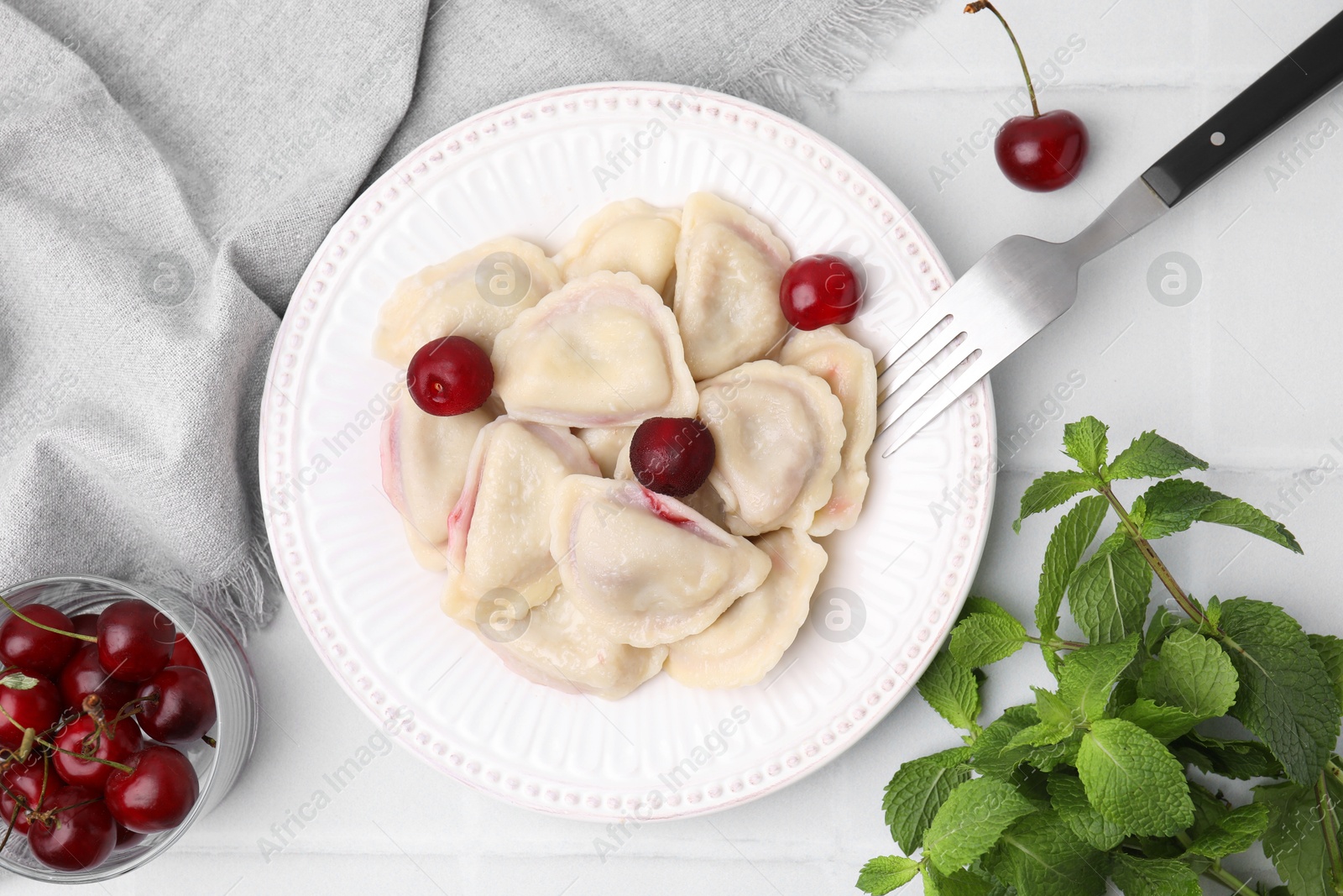 Photo of Traditional Ukrainian dumplings (varenyky) with cherries served on white tiled table, flat lay