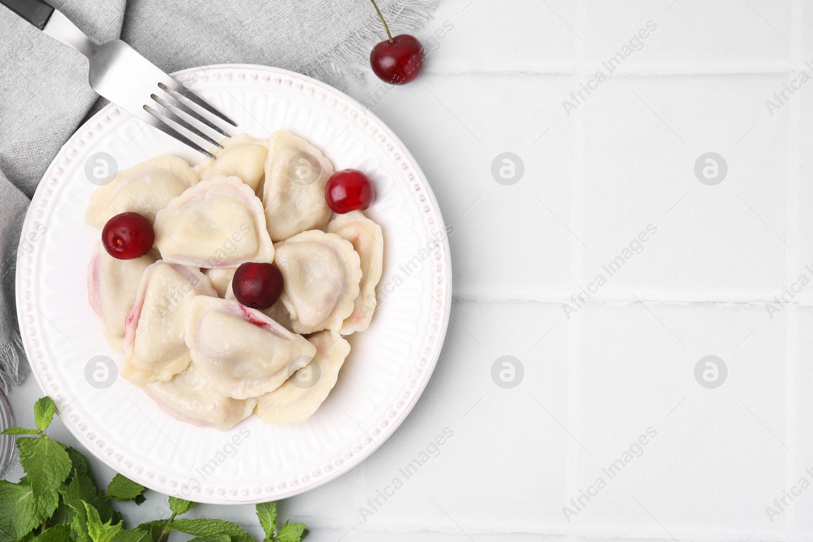 Photo of Traditional Ukrainian dumplings (varenyky) with cherries served on white tiled table, flat lay. Space for text