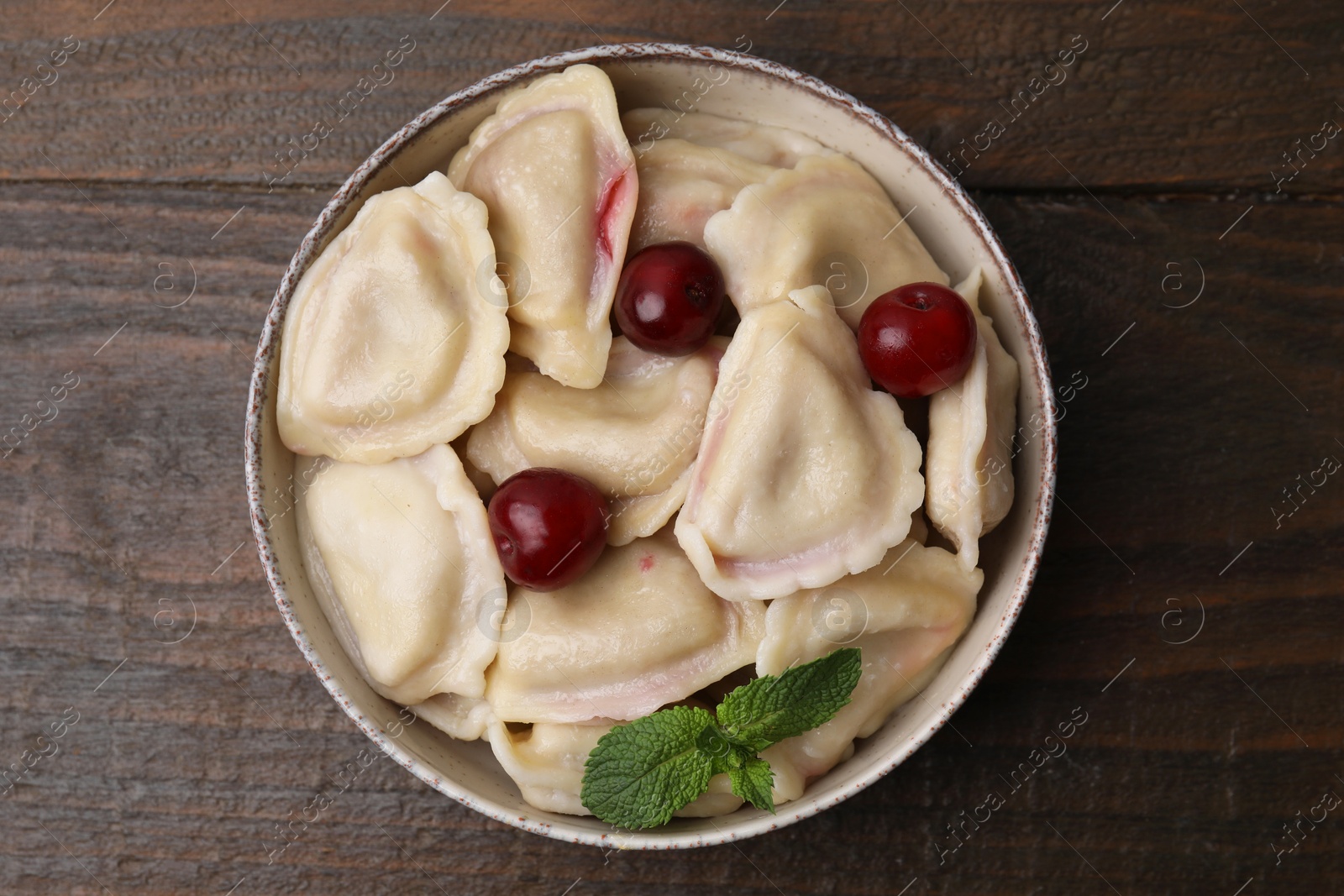 Photo of Traditional Ukrainian dumplings (varenyky) with cherries on wooden table, top view