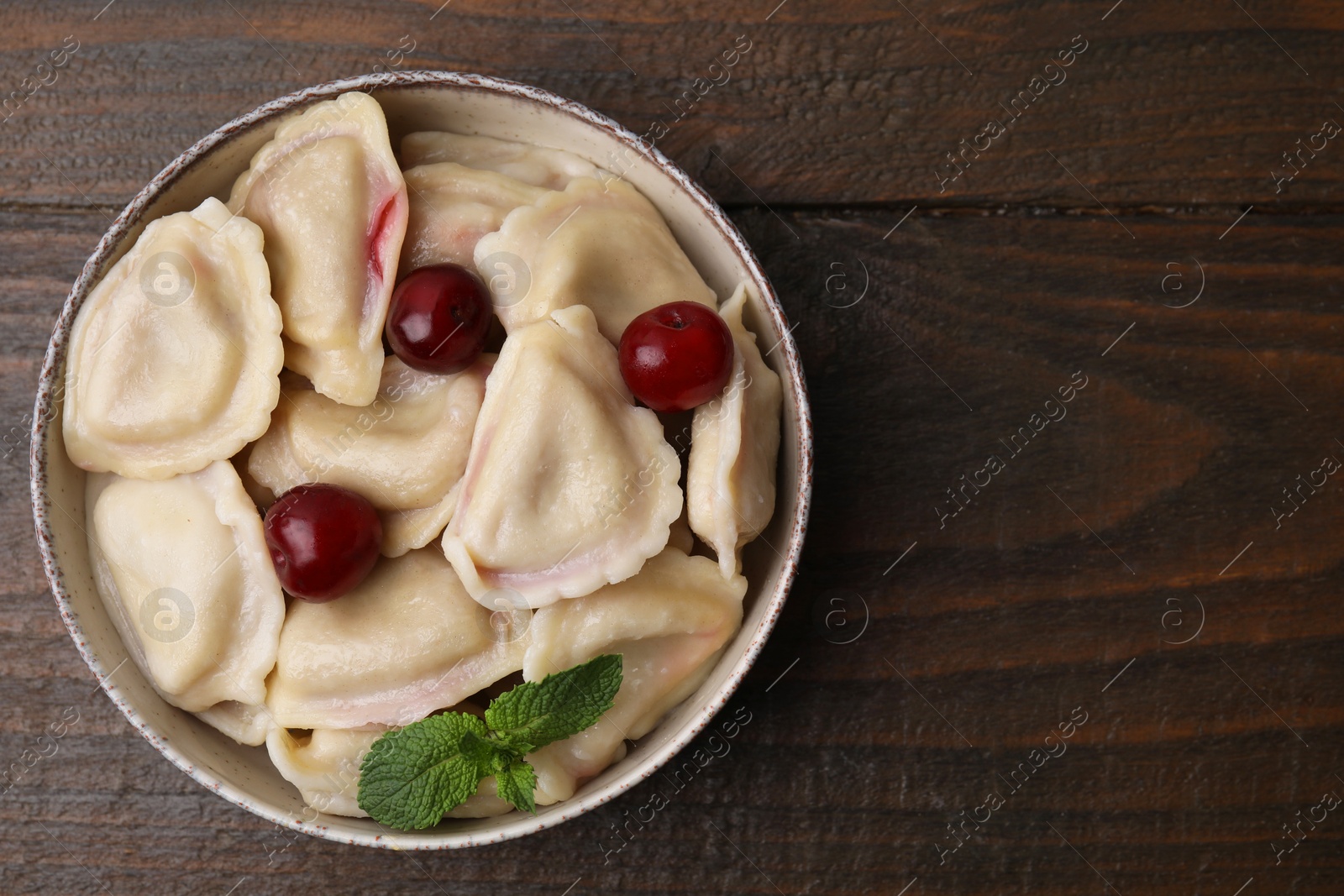 Photo of Traditional Ukrainian dumplings (varenyky) with cherries on wooden table, top view. Space for text