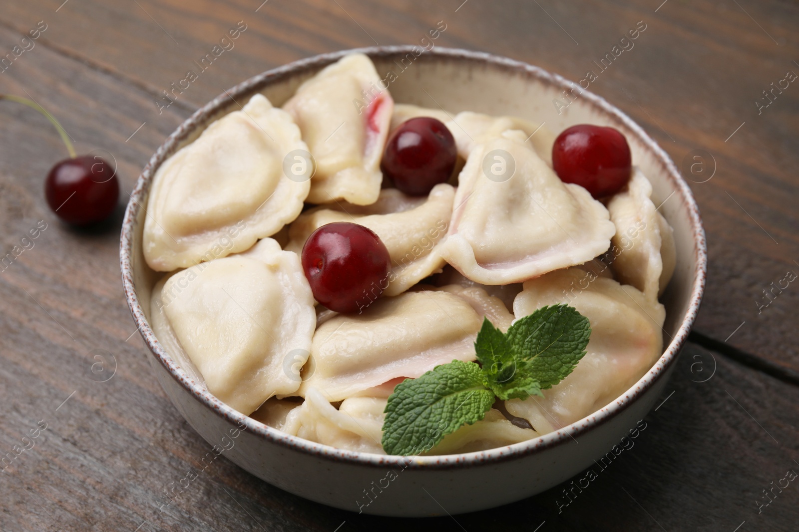 Photo of Traditional Ukrainian dumplings (varenyky) with cherries on wooden table, closeup