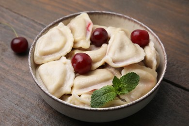 Photo of Traditional Ukrainian dumplings (varenyky) with cherries on wooden table, closeup