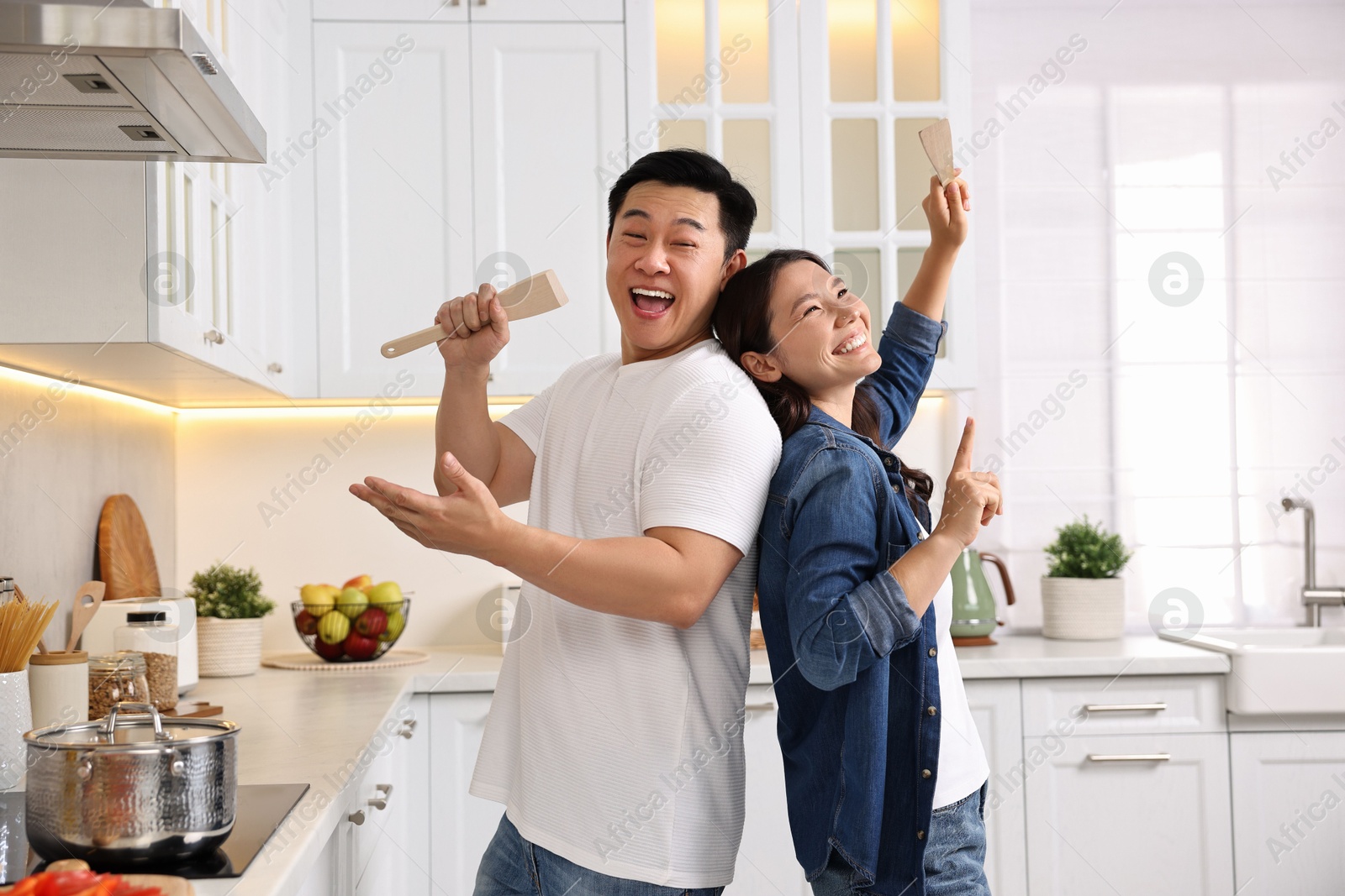 Photo of Happy lovely couple singing together while cooking in kitchen