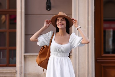 Photo of Beautiful young woman in stylish hat with backpack on city street