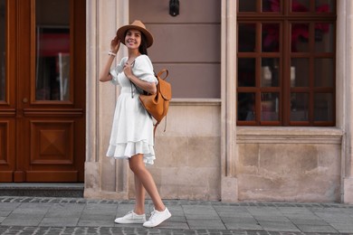 Beautiful young woman in stylish hat with backpack on city street