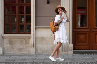 Beautiful young woman in stylish hat with backpack on city street