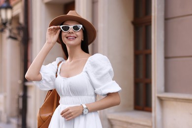 Smiling woman in stylish hat and sunglasses on city street