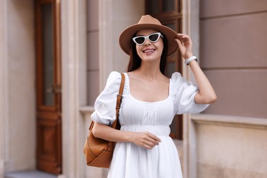 Smiling woman in stylish hat and sunglasses on city street