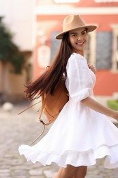 Photo of Beautiful young woman in stylish hat with backpack on city street