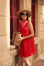 Photo of Smiling young woman in stylish hat, sunglasses and bag on city street