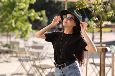 Young woman in stylish black hat and sunglasses on city street