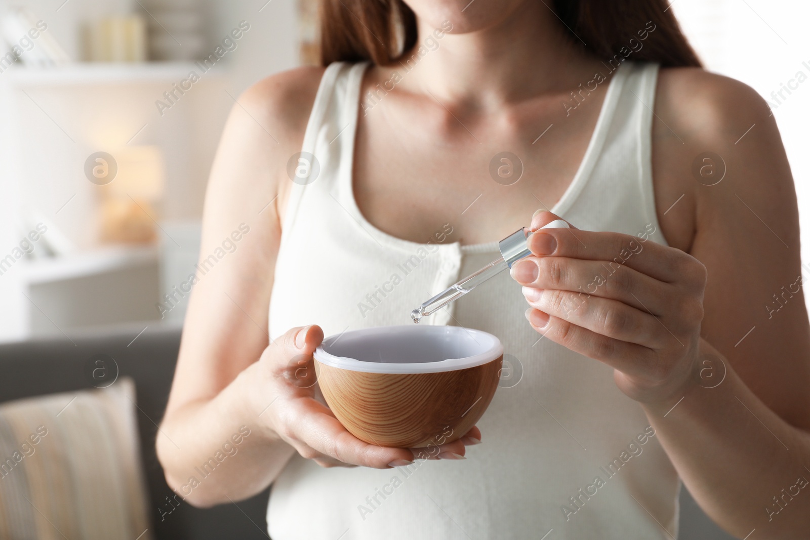 Photo of Woman adding essential oil to aroma diffuser at home, closeup