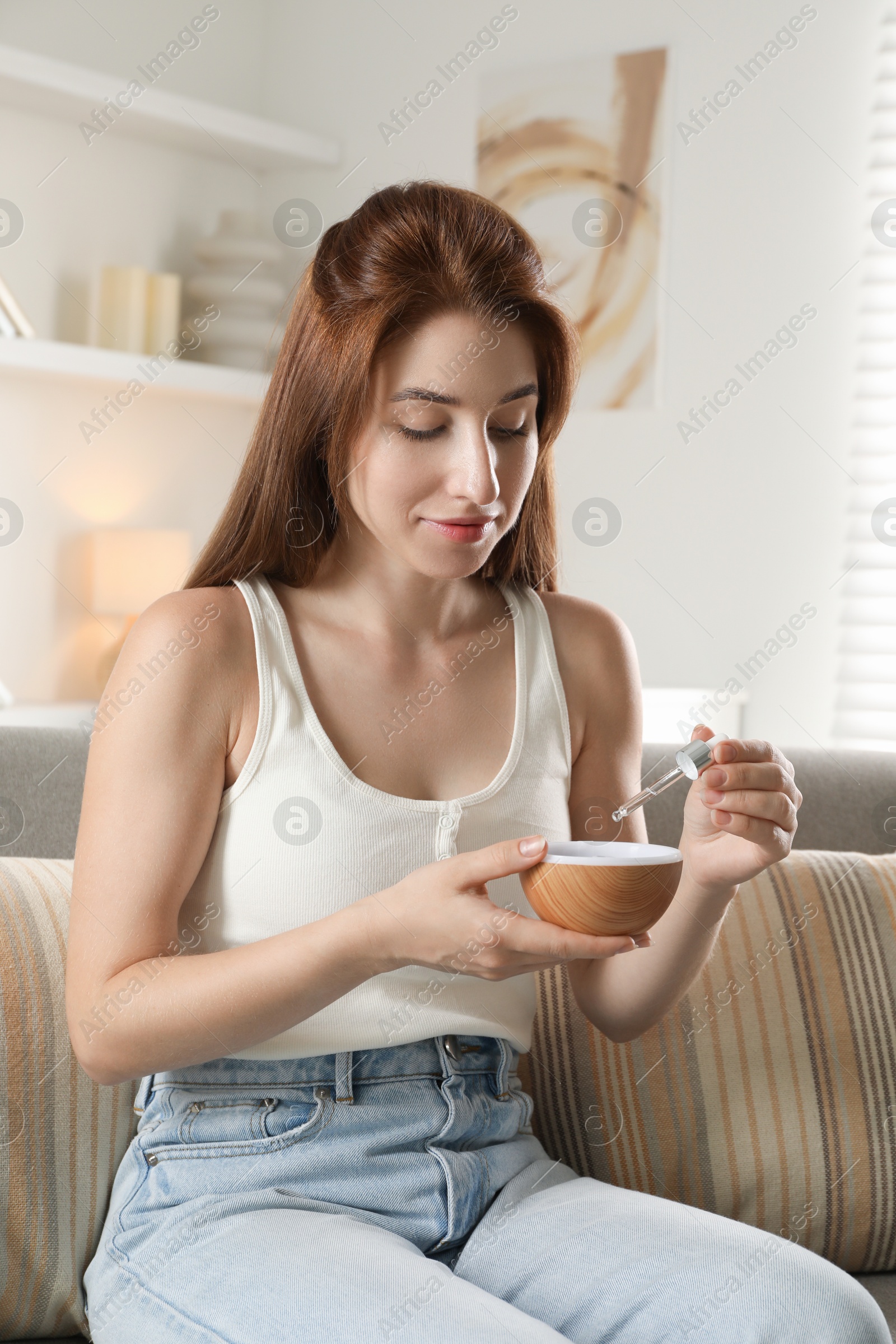 Photo of Woman adding essential oil to aroma diffuser at home