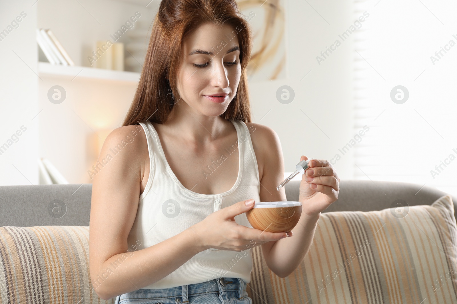 Photo of Woman adding essential oil to aroma diffuser at home