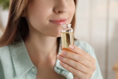 Woman with bottle of essential oil at home, closeup