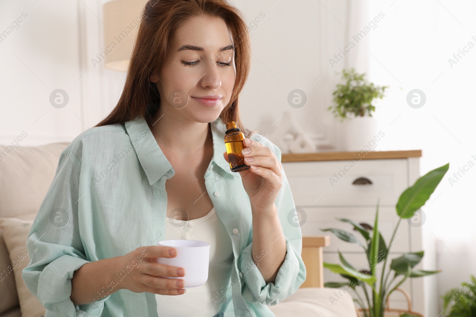 Photo of Woman with bottle of essential oil and aroma diffuser at home