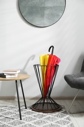 Colorful umbrella in stand, chair and coffee table indoors