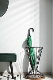 Green umbrella in stand near light wall