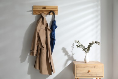 Photo of Colorful umbrella and trench coat hanging on rack at home