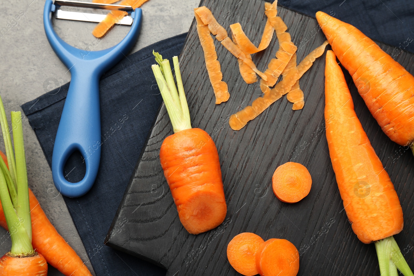 Photo of Fresh carrots, vegetable peeler and peels on gray textured table, flat lay