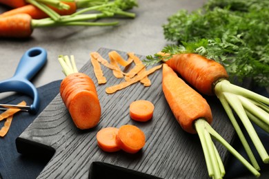 Photo of Fresh carrots, vegetable peeler and peels on gray table, closeup