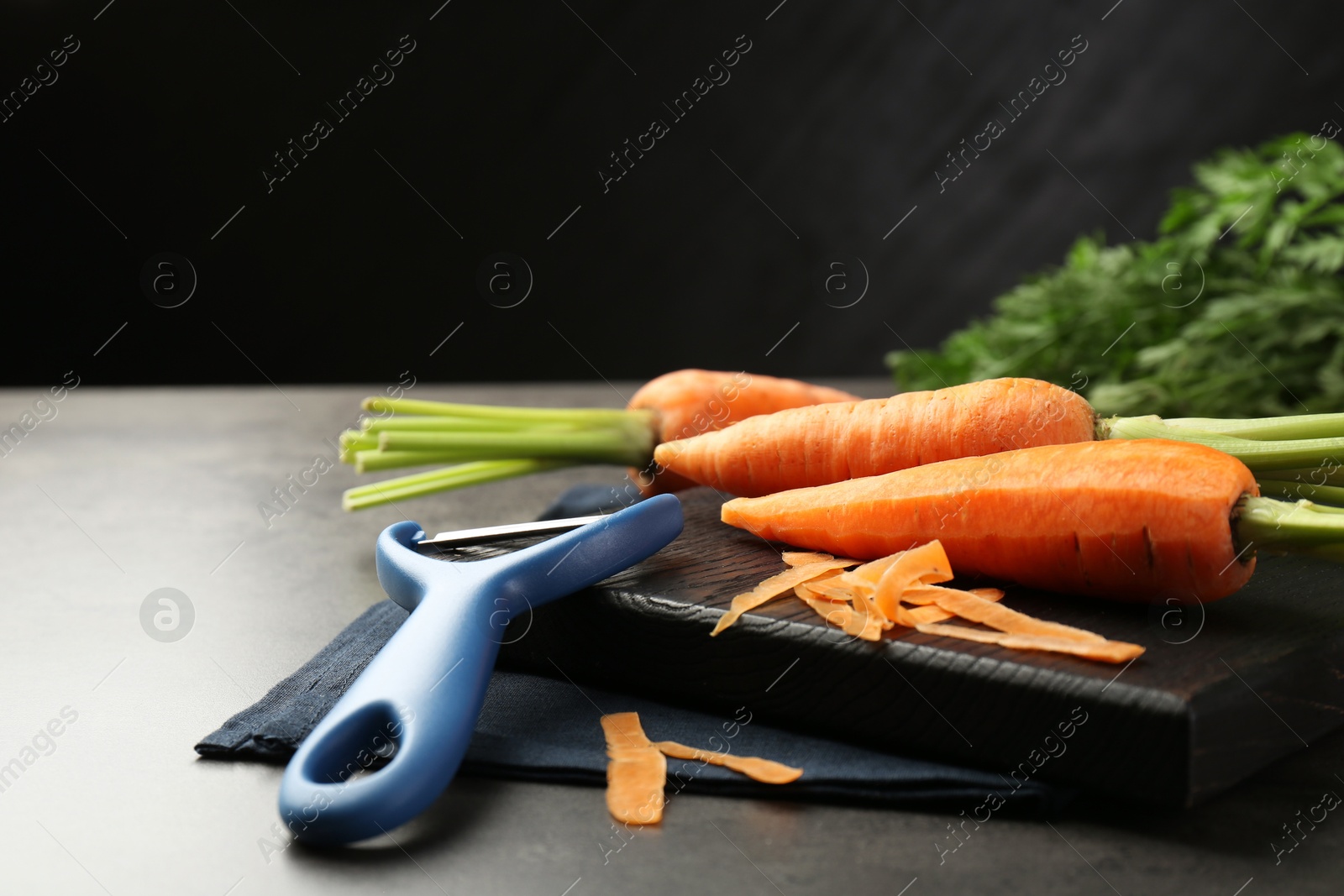 Photo of Fresh carrots, vegetable peeler and peels on gray textured table, closeup