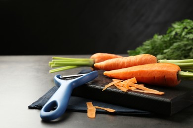 Photo of Fresh carrots, vegetable peeler and peels on gray textured table, closeup