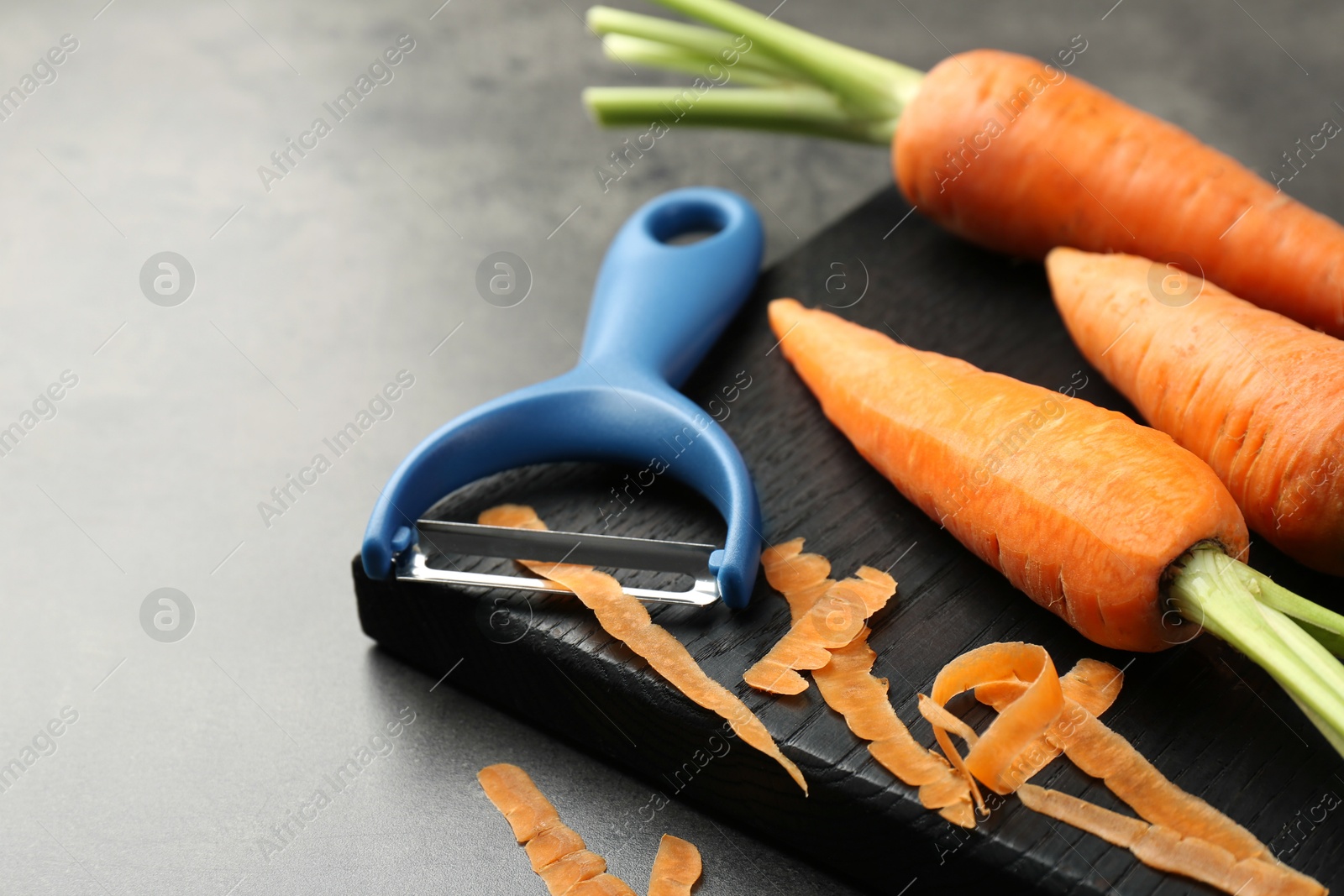 Photo of Fresh carrots, vegetable peeler and peels on gray textured table, closeup