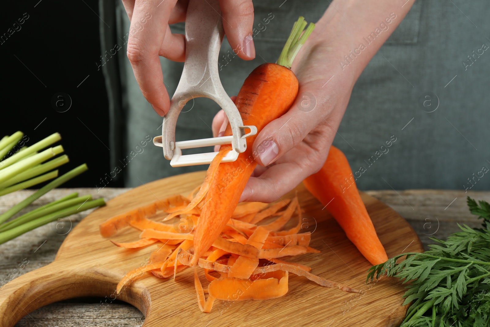 Photo of Woman peeling fresh carrot at wooden table, closeup