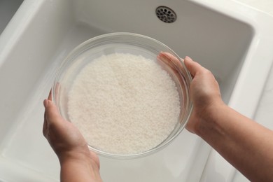 Photo of Woman holding bowl with rice and water above sink, closeup