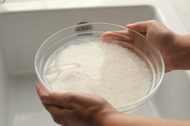 Photo of Woman holding bowl with rice and water above sink, closeup