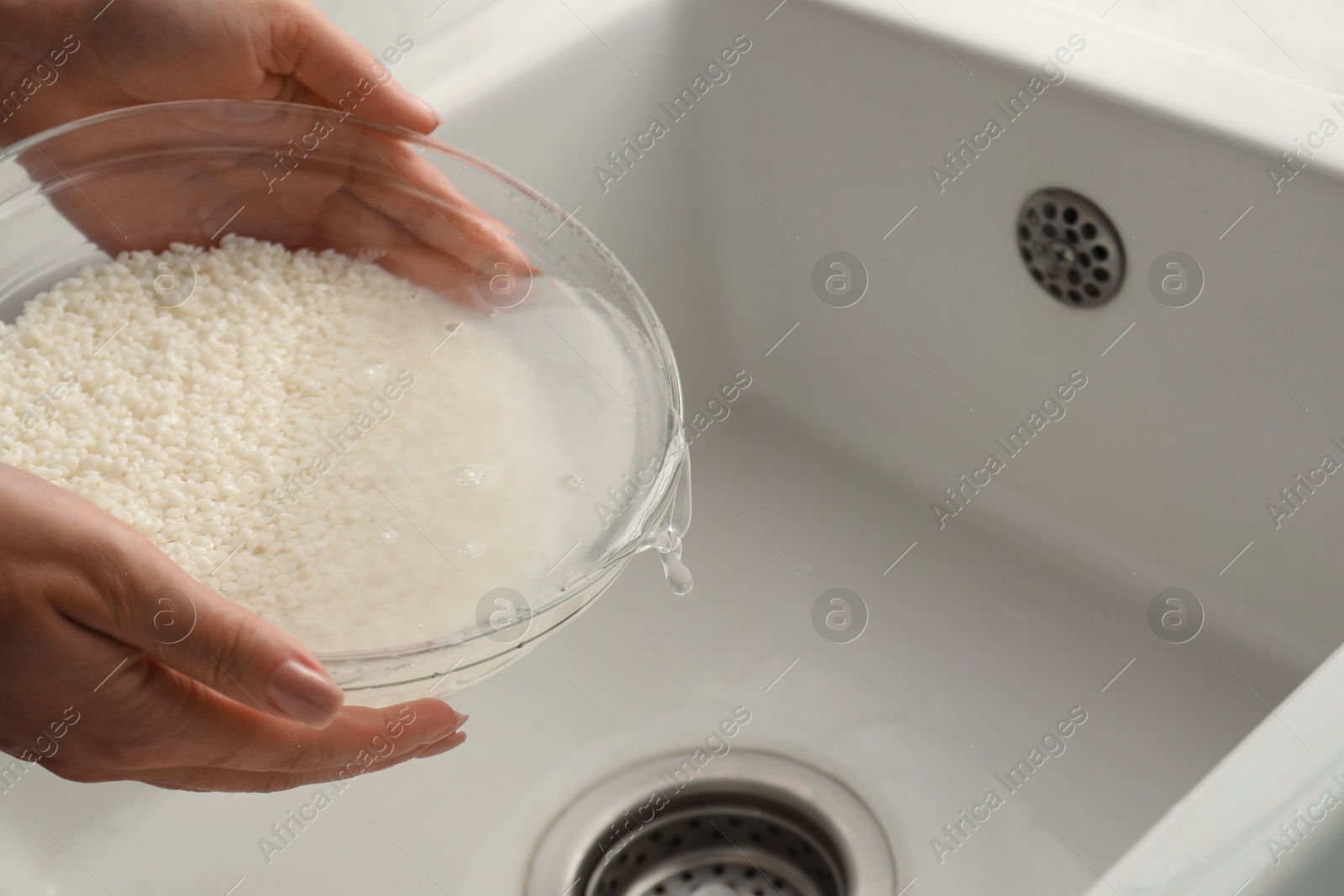 Photo of Woman rinsing rice in bowl above sink, closeup