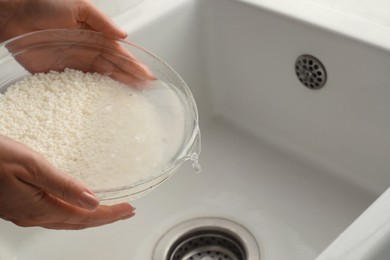 Woman rinsing rice in bowl above sink, closeup