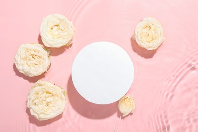 Photo of Beautiful rose flowers and round shaped podium in water on pink background, flat lay