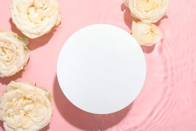 Photo of Beautiful rose flowers and round shaped podium in water on pink background, flat lay