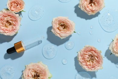 Photo of Beautiful rose flowers, pipette and drops of cosmetic serum on light blue background, flat lay