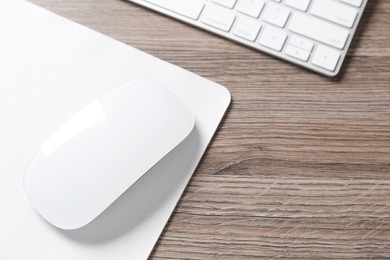 Photo of Computer mouse with mousepad and keyboard on wooden desk, closeup