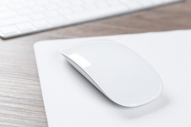 Photo of Computer mouse with mousepad and keyboard on wooden desk, closeup